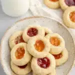 Stack of thumbprint cookies with glossy jam centers in ceramic bowl