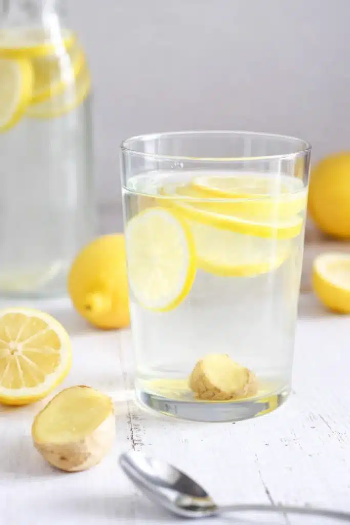 Glass of lemon ginger water with lemon slices and fresh ginger on rustic table