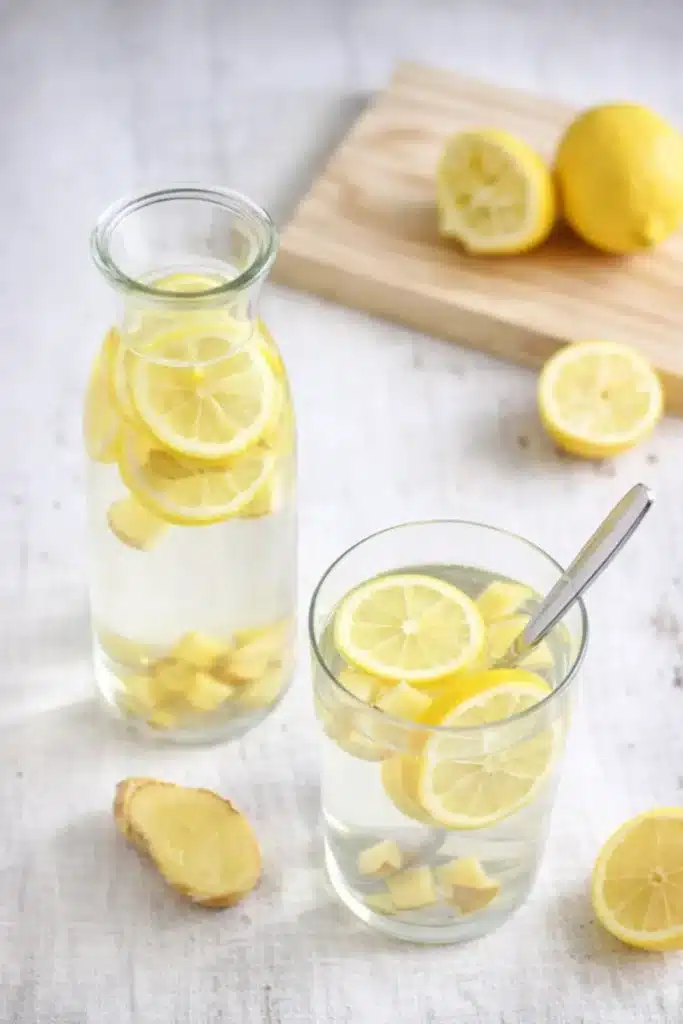 Glass and carafe of lemon ginger water on linen surface with sliced lemons