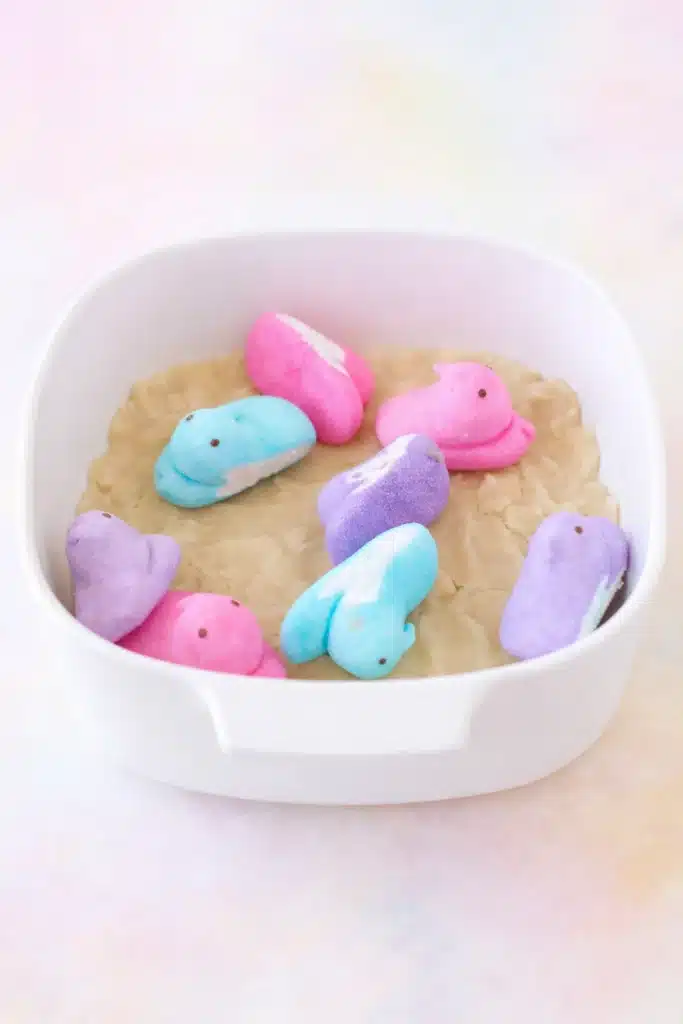 Easter Peeps Sugar Cookie Bars Recipe 8 Peeps sugar cookie bars recipe showing colorful Peeps arranged on cookie dough in a white baking dish.