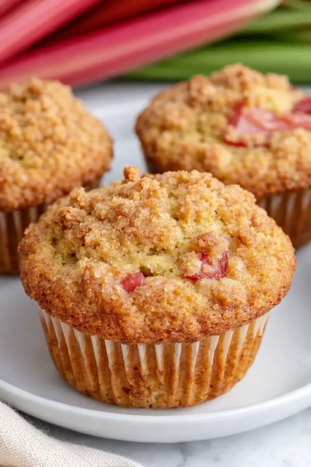 Golden rhubarb streusel muffins with crumb topping on ceramic plate
