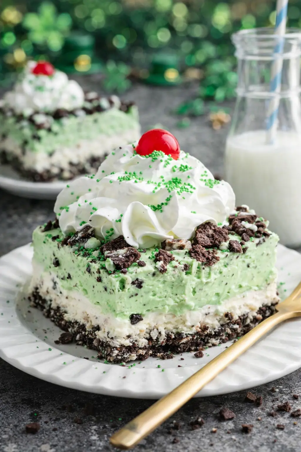 Shamrock lasagna slice with mint green layers, Oreo crust, whipped cream, and cherry on white plate