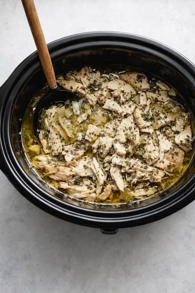 Slow Cooker Greek Chicken simmering in broth inside black slow cooker