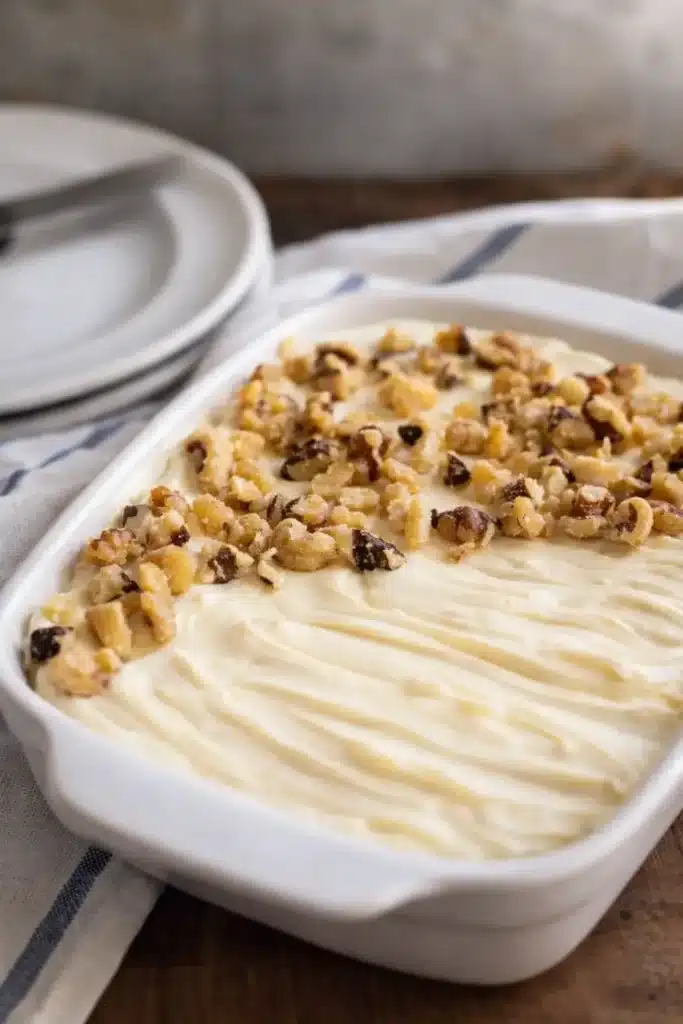 Small carrot cake with cream cheese frosting and walnuts in white dish