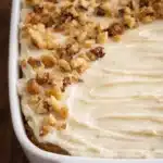 Small carrot cake with cream cheese frosting and walnuts in white dish