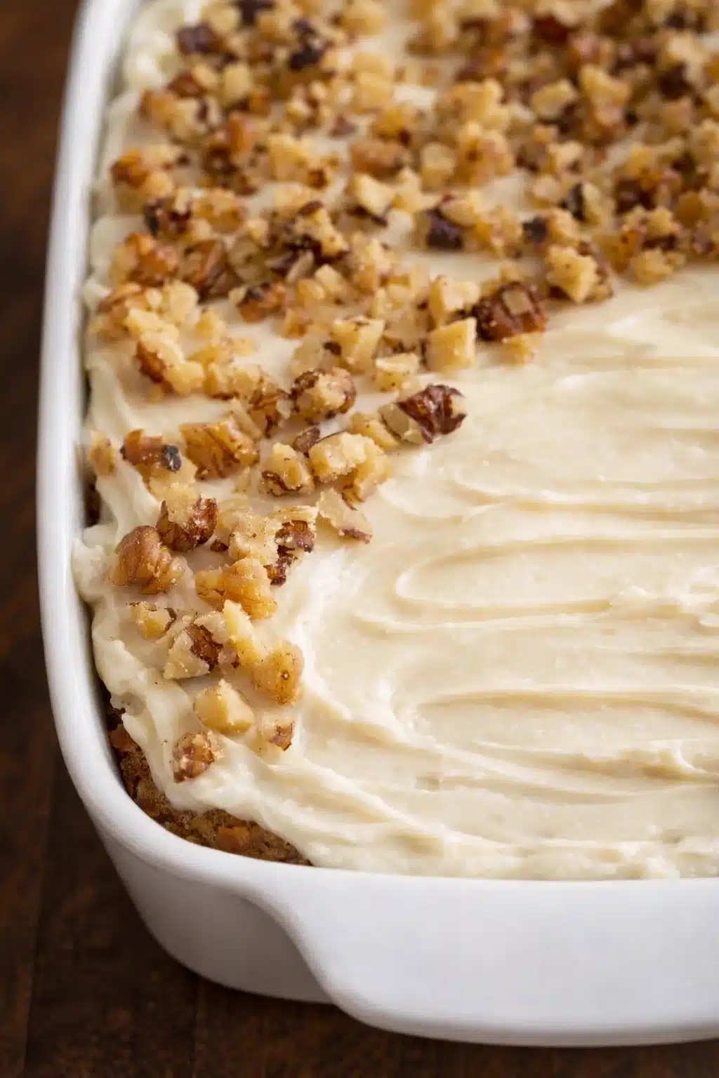 Small carrot cake with cream cheese frosting and walnuts in white dish