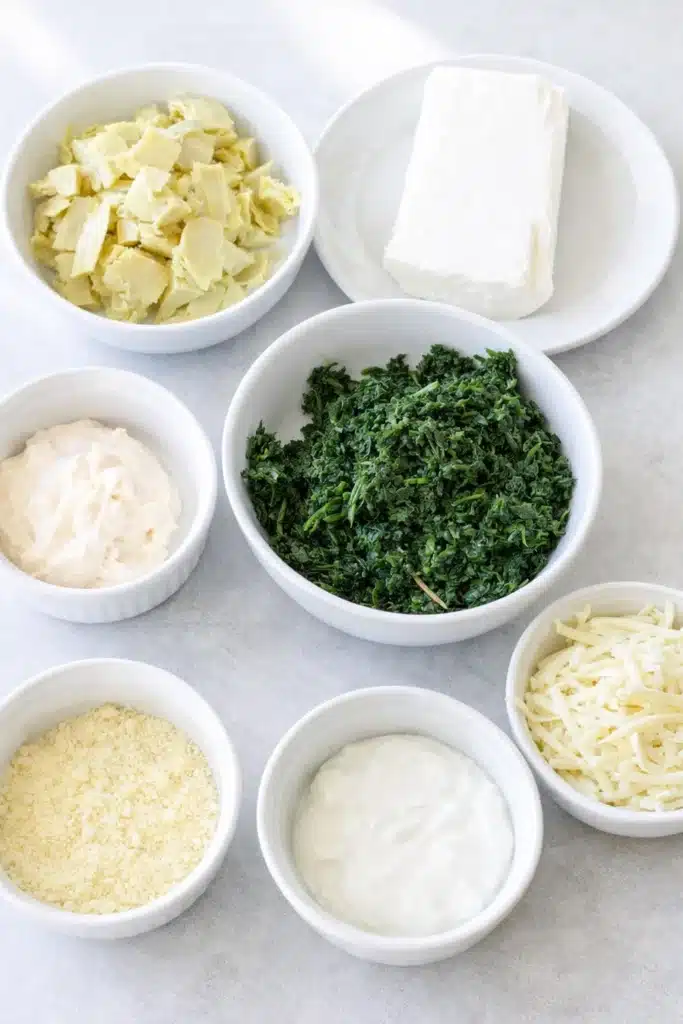 Spinach artichoke dip ingredients in white bowls on gray table