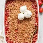 Strawberry rhubarb crisp with oat topping and vanilla ice cream in baking dish