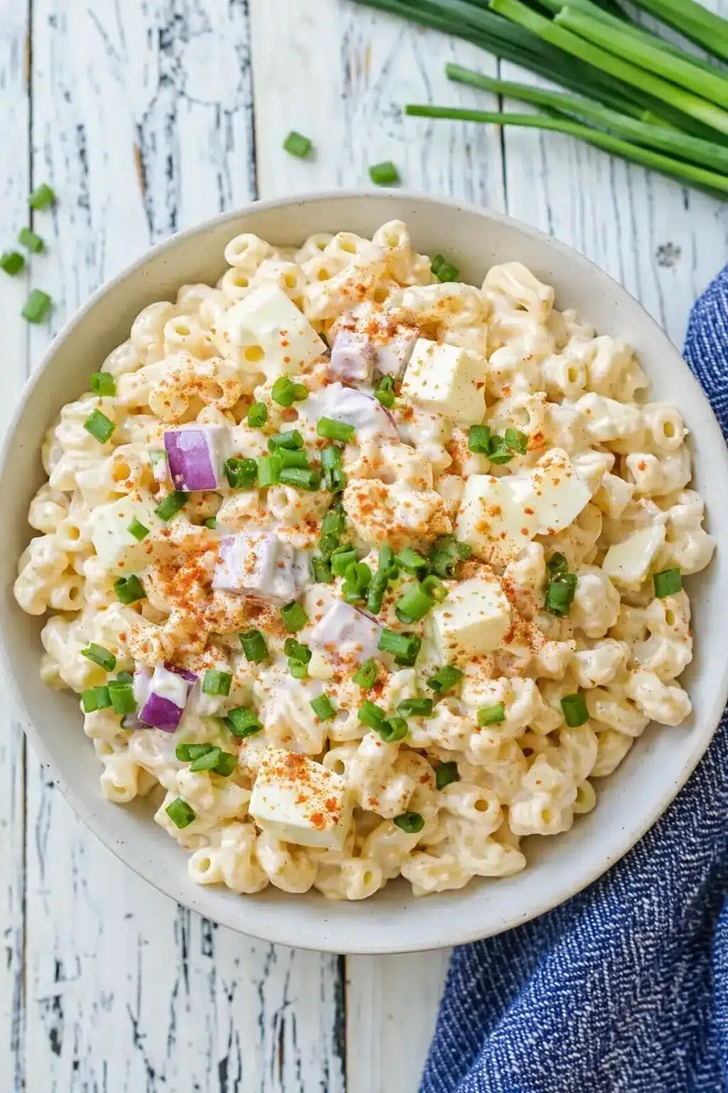 Creamy deviled eggs pasta salad with paprika and green onions in a white bowl