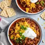 Two bowls of homemade chili topped with cheese, sour cream, and green onions