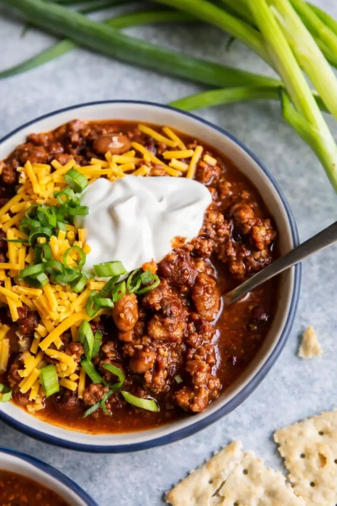 Bowl of homemade chili with cheese, sour cream, and green onions