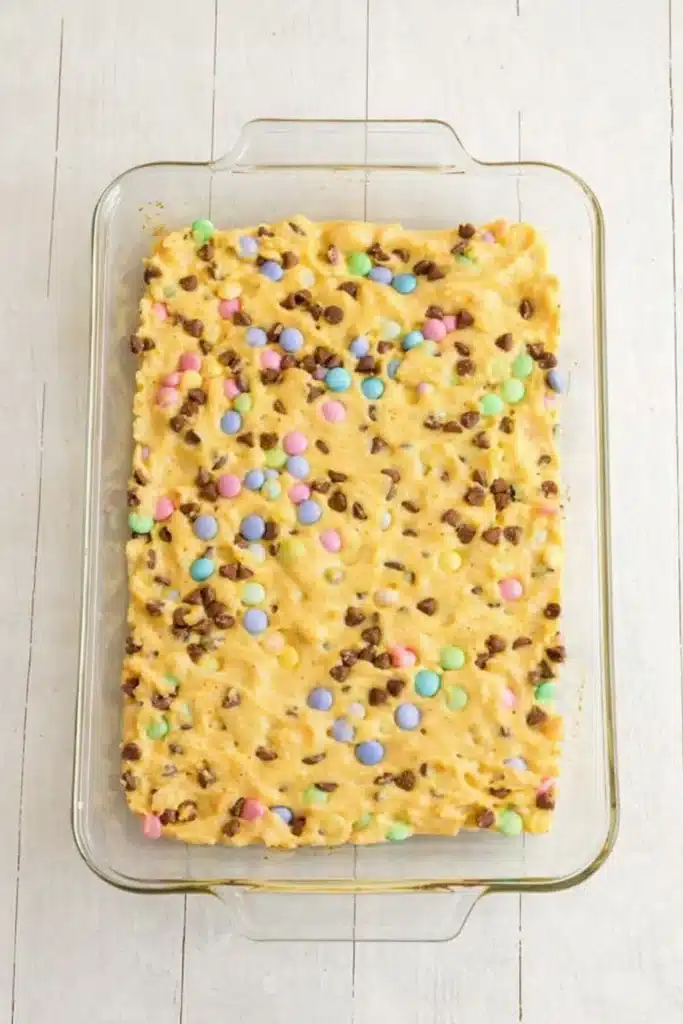 Easter Cake Mix Cookie Bars – Simple, Chewy, and Delicious 7 Unbaked Easter cake mix cookie bar batter in glass baking dish with pastel M&Ms