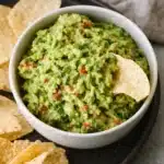 Chunky homemade guacamole dip in a bowl with crispy tortilla chips