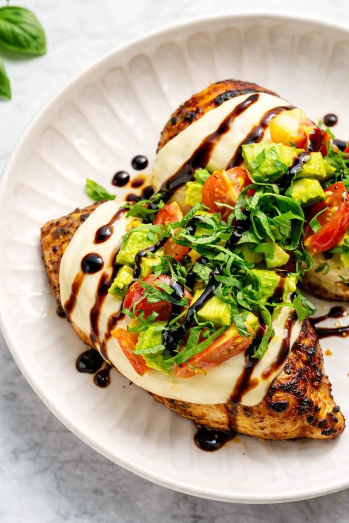 California grilled chicken with mozzarella avocado tomatoes basil and balsamic glaze on a white plate