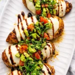 California grilled chicken with mozzarella, avocado, tomatoes, basil and balsamic glaze on a white serving platter.