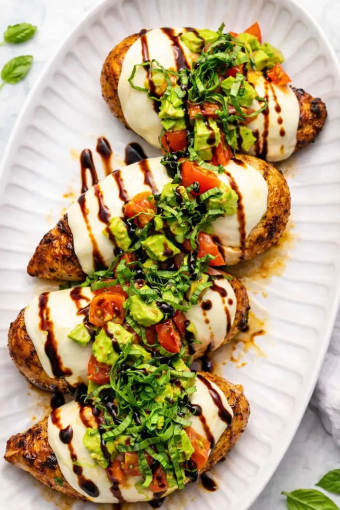 California grilled chicken with mozzarella, avocado, tomatoes, basil and balsamic glaze on a white serving platter.