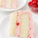 Cherry almond cake slice with pink cherry buttercream frosting on a white plate
