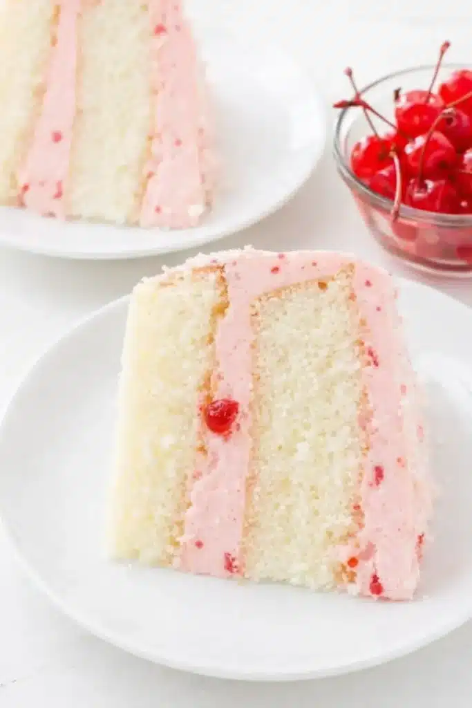 Cherry almond cake slice with pink cherry buttercream frosting on a white plate