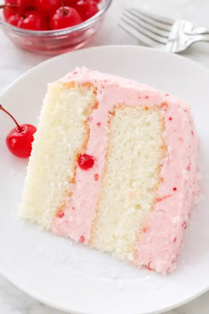 Cherry almond cake slice with pink cherry buttercream frosting on a white plate
