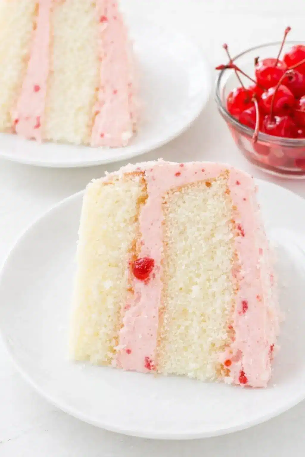 Cherry almond cake slice with pink cherry buttercream frosting on a white plate