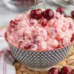 Cherry cheesecake fluff dessert in a bowl topped with fresh cherries and creamy pink texture