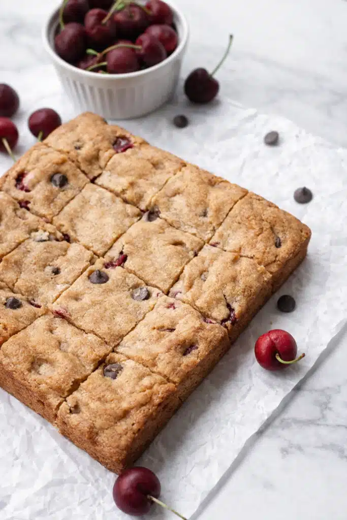 Cherry chocolate chip blondies baked in a pan and cut into squares on parchment paper