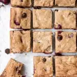 Cherry chocolate chip blondies cut into squares with visible cherries and chocolate chips on parchment paper