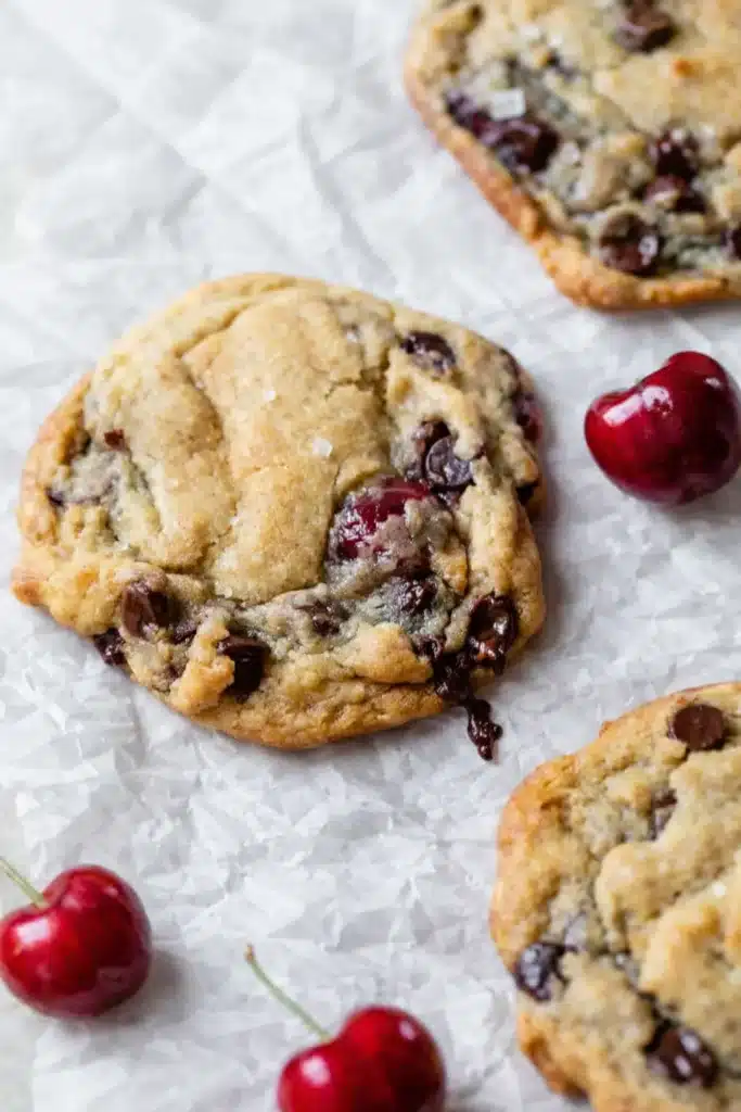 Cherry chocolate chip cookies with fresh cherries and melted chocolate chips on baking paper