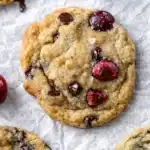Cherry chocolate chip cookies with fresh cherries and melted chocolate chips on a baking surface