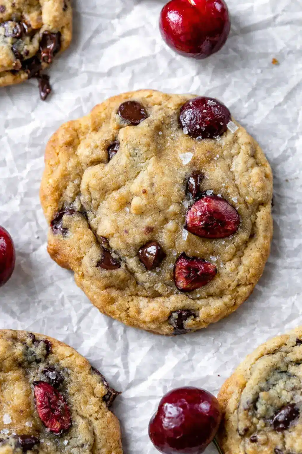 Cherry chocolate chip cookies with fresh cherries and melted chocolate chips on a baking surface