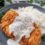 Chicken fried chicken with creamy country gravy served with mashed potatoes on a rustic plate