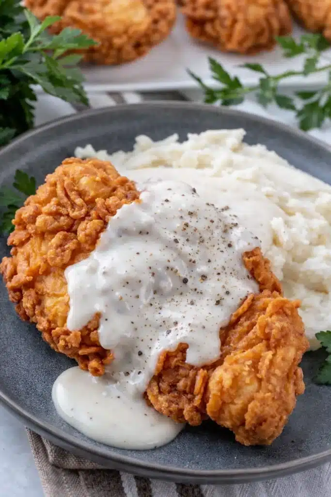 Chicken fried chicken with creamy country gravy served with mashed potatoes on a rustic plate