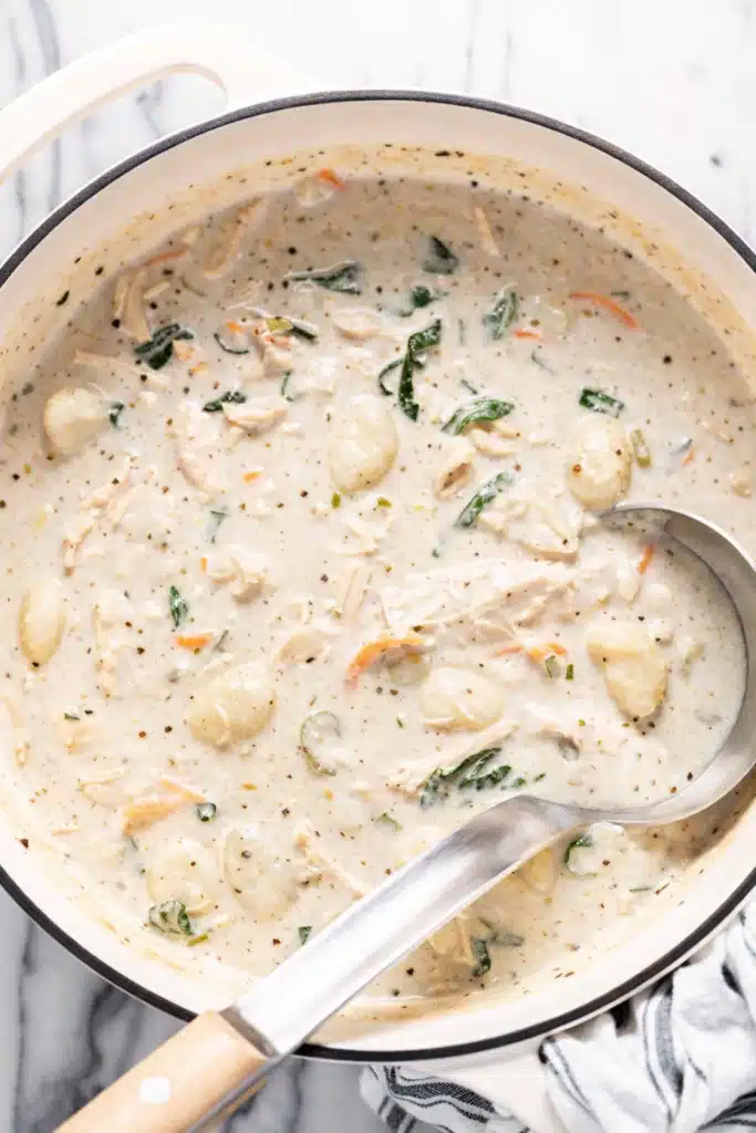 Creamy chicken gnocchi soup cooking in a pot with shredded chicken, spinach, and potato gnocchi