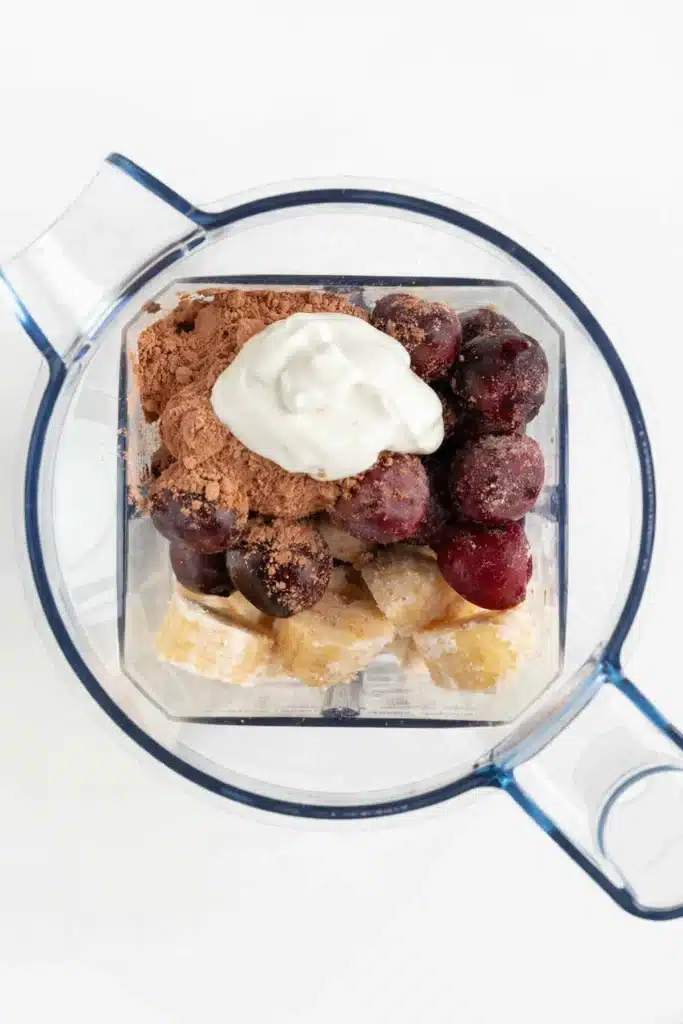 Chocolate Cherry Smoothie Bowl ingredients in blender with banana, cherries, cocoa powder and yogurt