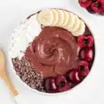 Chocolate cherry smoothie bowl topped with banana slices, fresh cherries, coconut flakes and cacao nibs
