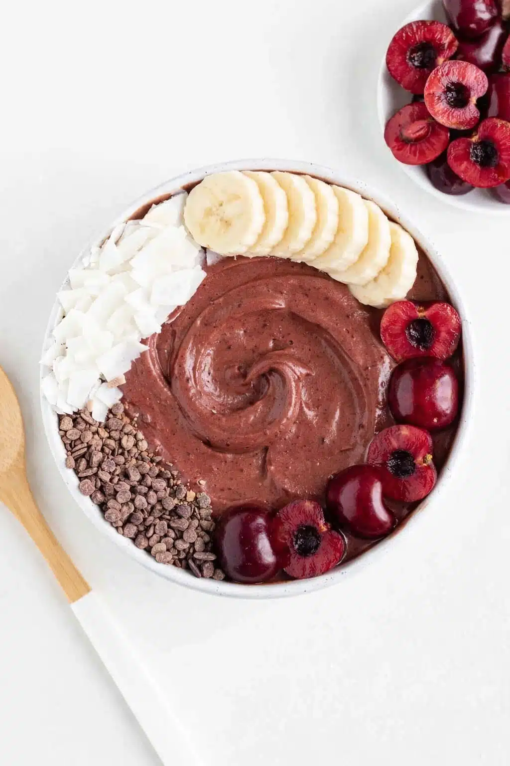 Chocolate cherry smoothie bowl topped with banana slices, fresh cherries, coconut flakes and cacao nibs