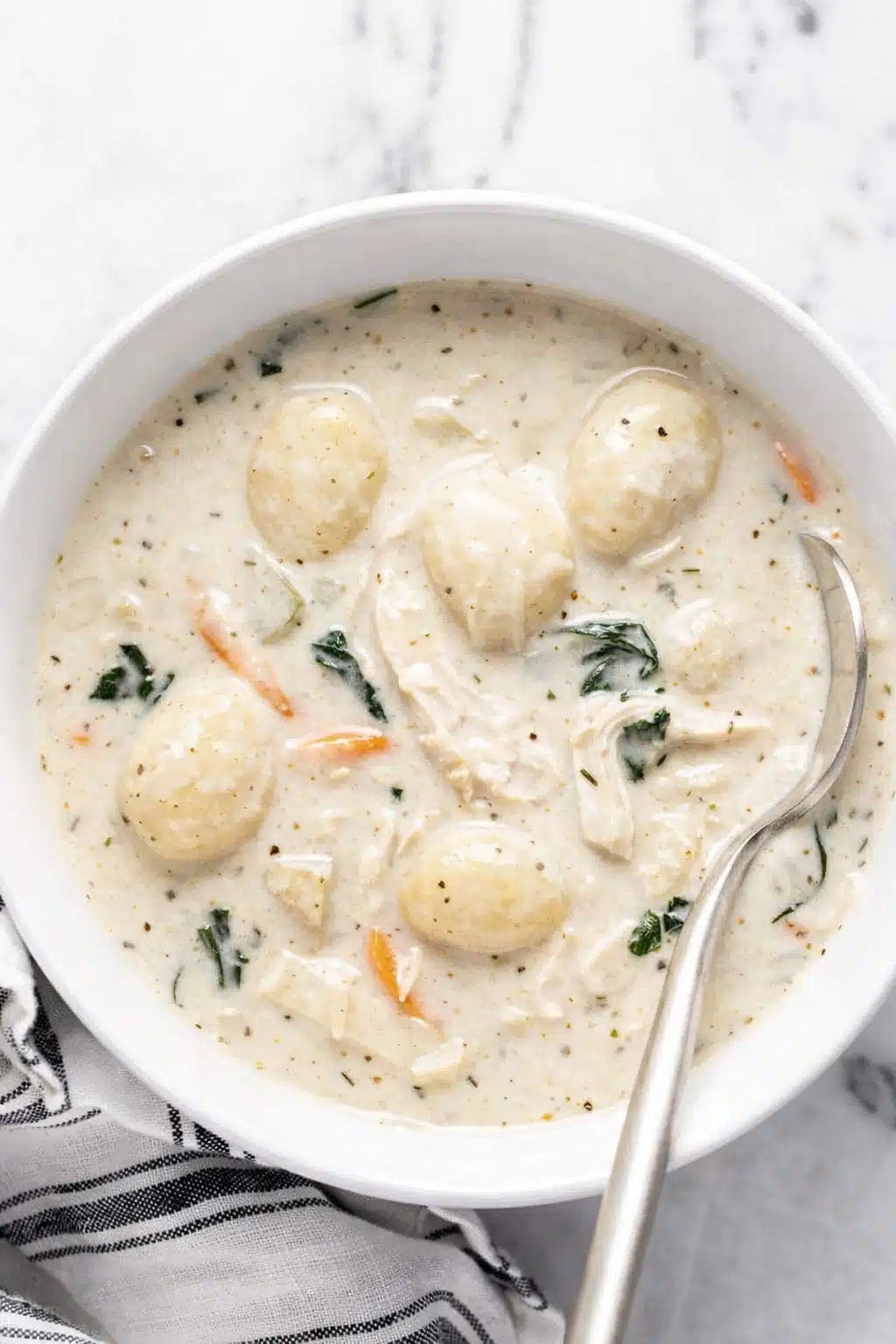 Creamy chicken gnocchi soup with shredded chicken, spinach, carrots, and potato gnocchi in a white bowl