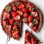 Dark chocolate strawberry tart with glossy ganache and fresh strawberries on marble surface