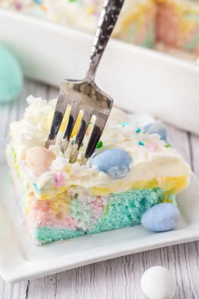 Easter Poke Cake Simple Colorful Easter Dessert 7 Easter poke cake slice with pastel layers, whipped cream, coconut, and candy eggs