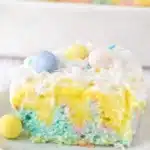 Slice of colorful Easter poke cake with vanilla pudding, whipped cream, coconut, and pastel candy eggs