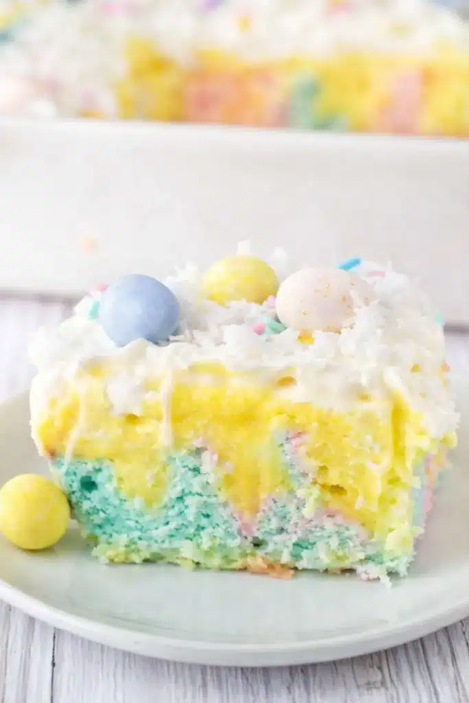 Slice of colorful Easter poke cake with vanilla pudding, whipped cream, coconut, and pastel candy eggs