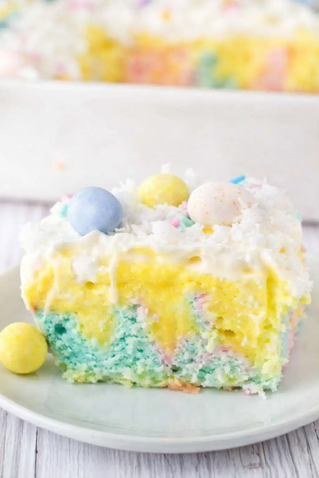 Slice of colorful Easter poke cake with vanilla pudding, whipped cream, coconut, and pastel candy eggs
