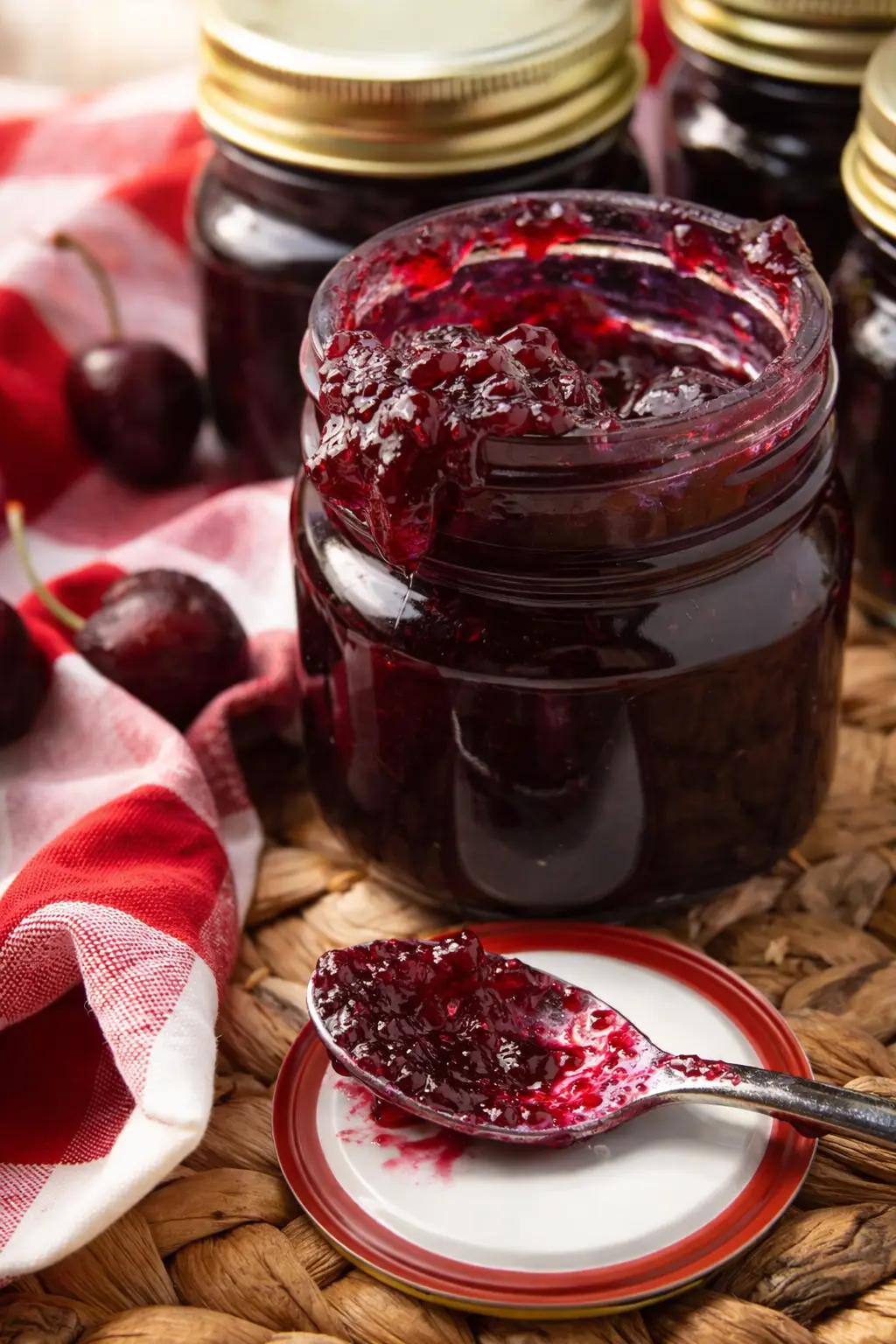 Homemade cherry vanilla jam in glass jar with spoon and fresh cherries on rustic table