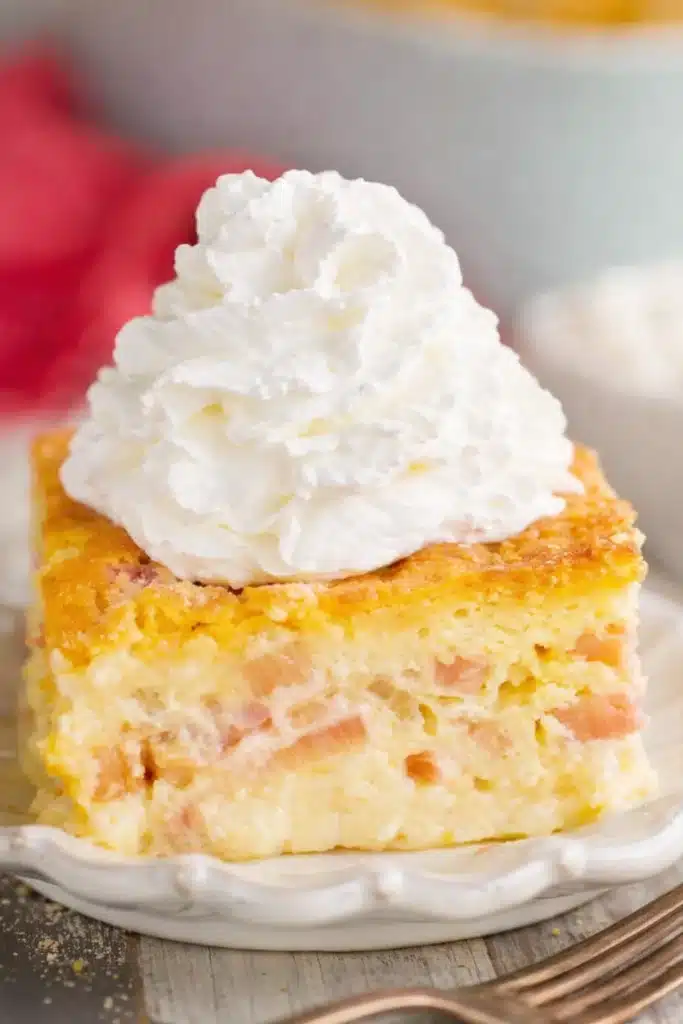 Easy rhubarb custard cake slice with whipped cream on a dessert plate