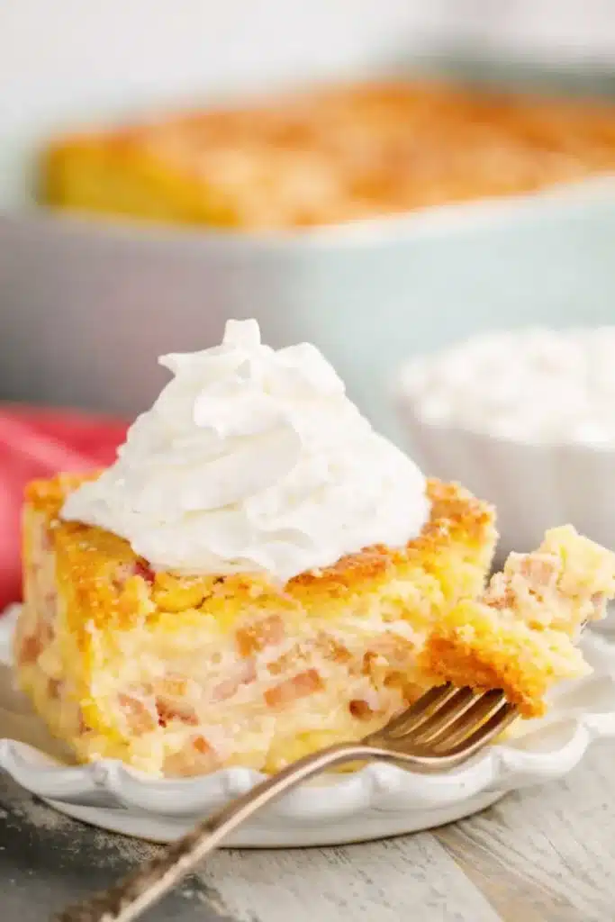 Easy Rhubarb Custard Cake slice with whipped cream and fork