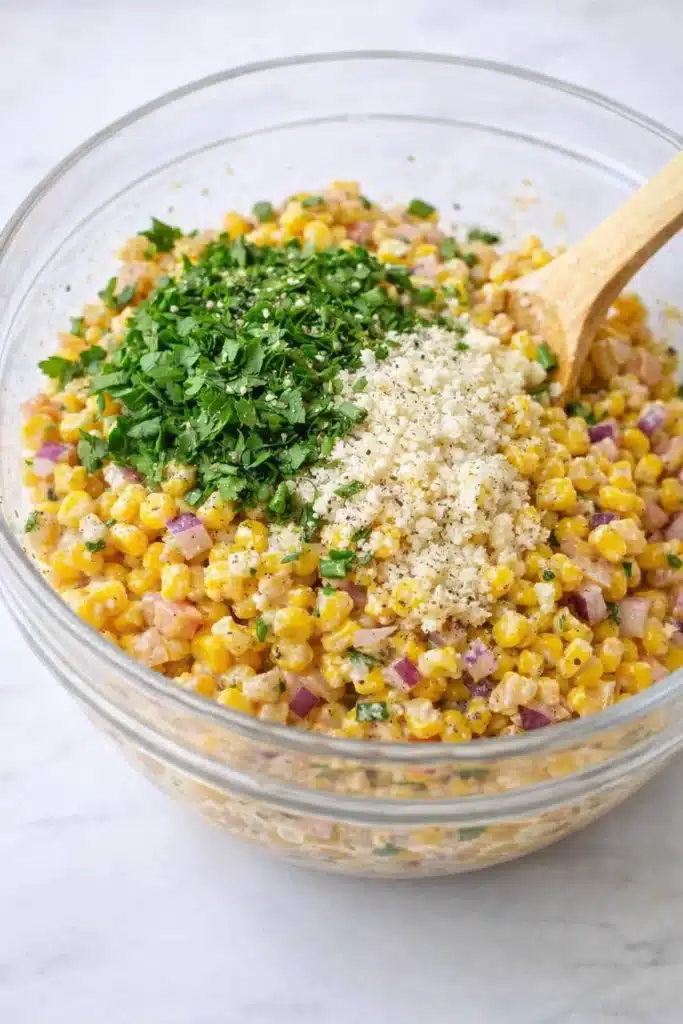Elote corn salad ingredients with cotija cheese cilantro and corn in mixing bowl