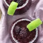 Frozen blackberry margarita with lime wedge and salted rim in a glass with frozen berries