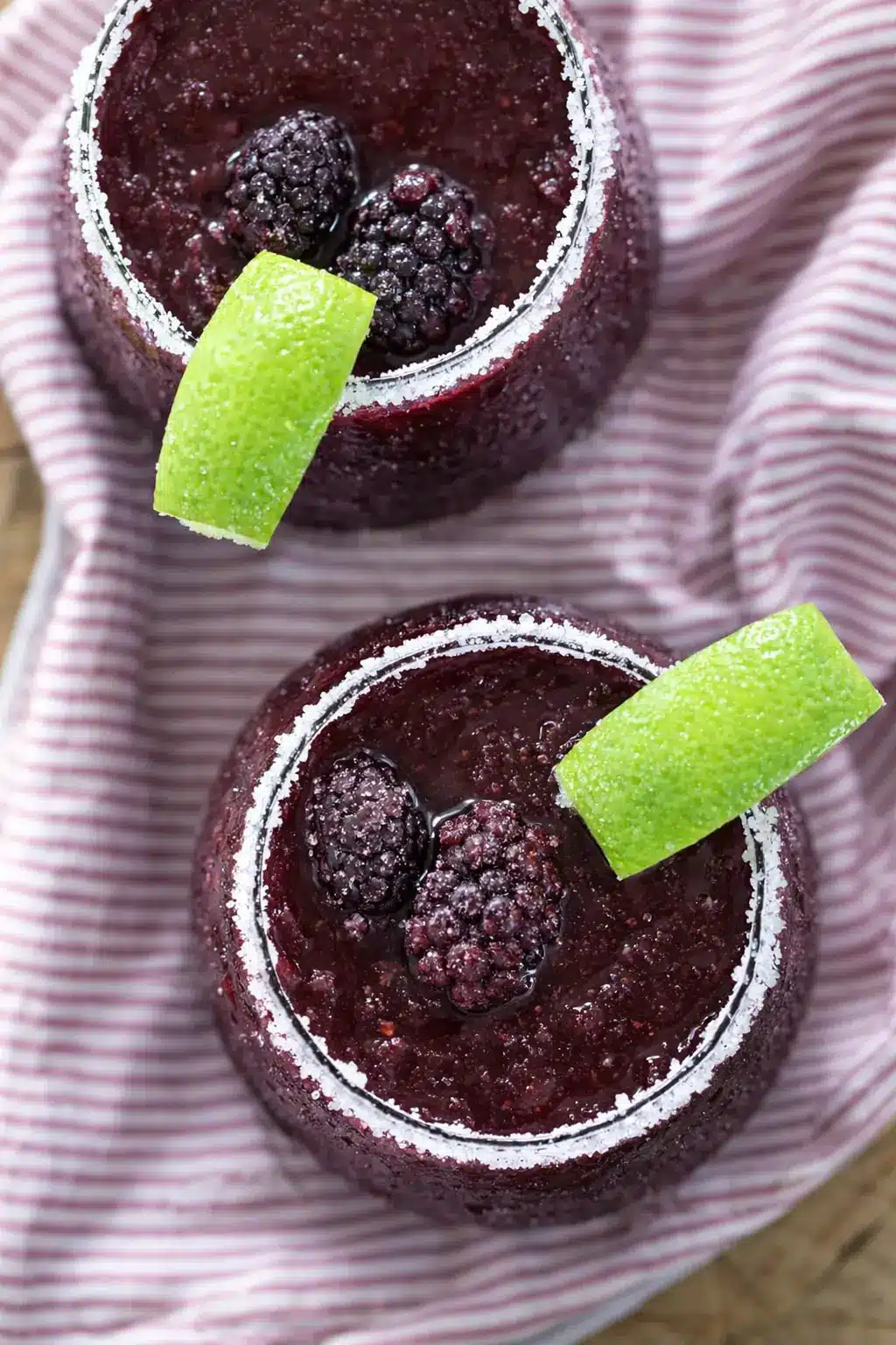 Frozen blackberry margarita with lime wedge and salted rim in a glass with frozen berries