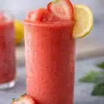 Frozen strawberry lemonade slushy drink in a tall glass with lemon slice and fresh strawberry garnish
