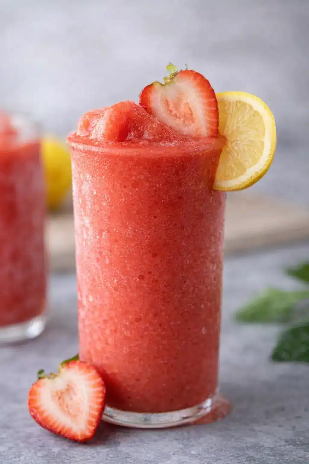 Frozen strawberry lemonade slushy drink in a tall glass with lemon slice and fresh strawberry garnish